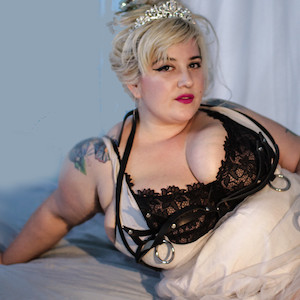 Photo of heavy, curvy Genevieve LaFleur reclining on a bed in a lace bra.