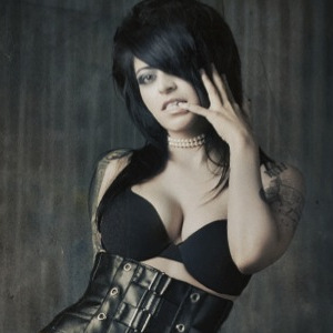 Studio portrait of Jane Jett posing in a black bra and cinch made of multiple belts. All black leather. Ouch.