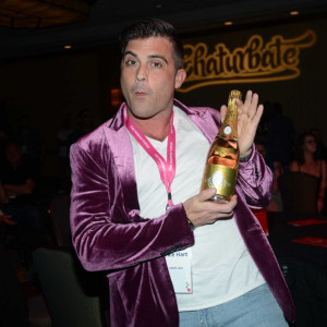 Lance Hart in a purple cashmere blazer goffing with a golden champagne bottle after his VOYEUR Awards win.
