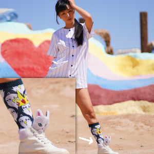 Marica Hase posing in a baseball shirt pyjama top and bare legs, wearing goofy Anime-character socks and sneakers. Cute!